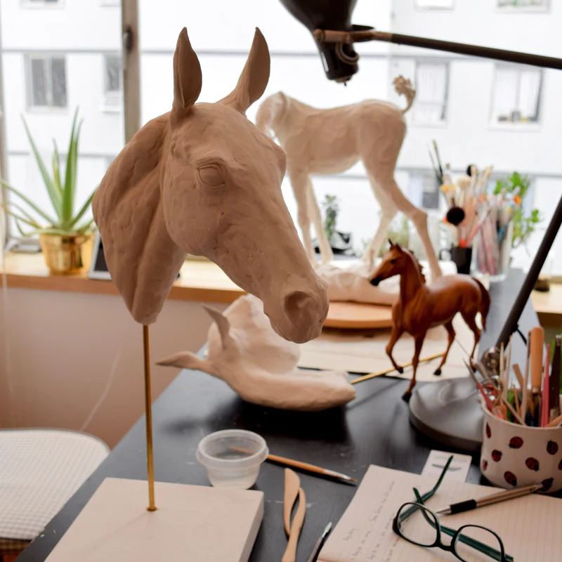Featured sculptor Susie Benes's work desk showcasing three in progress horse sculptures made with Creative Paperclay® alongside sculpting tools.